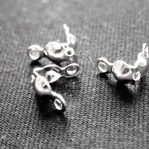 May include: Three silver-toned metal clasps for jewelry making. The clasps are shaped like a curved hook with a small loop on each end.