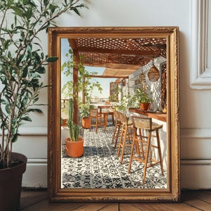 May include: A framed watercolor painting depicts an outdoor cafe scene. The painting features a pergola, bar stools, tables, and potted plants. The floor has a black and white tile pattern. The frame is gold-colored.