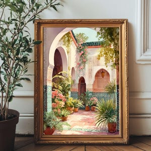 May include: A framed print showing an ornate courtyard with arched doorways, lush greenery, and potted plants. The artwork features a warm colour palette with terracotta tiles and detailed architectural elements, creating a serene and inviting scene.