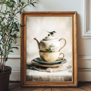 May include: A framed print of a vintage tea set. The tea set includes a teapot, teacup, and saucer, all in cream with green floral accents. A small bird perches on the teapot. The frame is gold, and the background is a soft, neutral color.