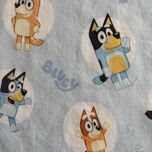 May include: Light blue fabric featuring cartoon dogs in various poses, each within a white circle. The dogs are primarily orange, blue, and black, with large eyes and friendly expressions. The word "Bluey" is printed in light blue.