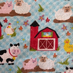 May include: A light blue fabric with a farm animal pattern. The design includes a red barn, cows, pigs, sheep, chickens, and ducks. The fabric has a fringed edge and is decorated with flowers.