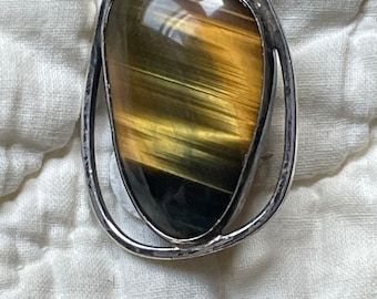 May include: A silver ring with a large, oval-shaped tiger's eye gemstone. The gemstone is a mix of brown, gold, and black.