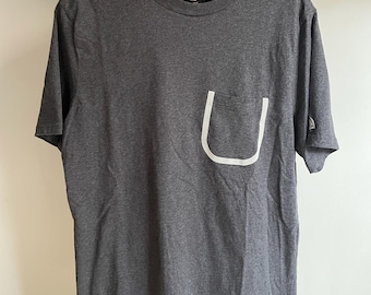 Camiseta tamanho ovo com bolso grande da Octobers. 53 cm de axila a axila. 76 cm de comprimento. Fita refletiva nos bolsos e remendo no braço.