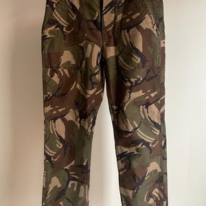 Peut inclure: Pantalon camouflage à jambe droite et coupe décontractée. Le pantalon est à motif camouflage marron, vert et noir.