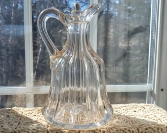 Peut inclure: Un pichet en verre transparent avec un motif côtelé et une poignée. Le pichet est posé sur une dentelle au crochet.