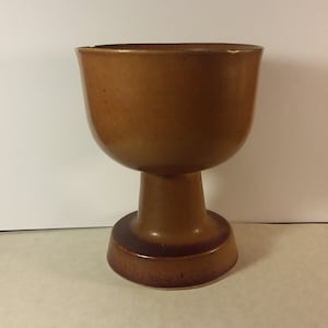 May include: A brown ceramic goblet with a wide base and a rounded bowl. The goblet is glazed in a rich brown color.