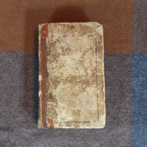 May include: A worn, brown leather-bound book with a red spine and a faded title on the front cover.