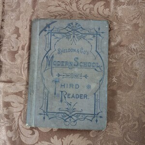 May include: A vintage book titled "Sheldon & Co's Modern School Third Reader" with a decorative design on the cover.