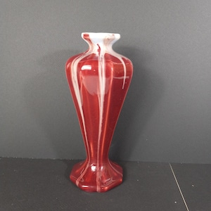 Peut inclure: Un vase en céramique rouge et blanc avec un motif géométrique. Le vase a une base large et un col étroit.