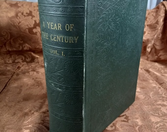 May include: A dark green hardcover book with gold lettering on the spine. The title is "A Year of the Century" and the volume number is "Vol. I."