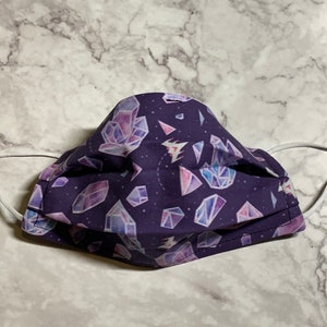 May include: A purple face mask with a repeating pattern of white and pink crystals on a dark purple background.