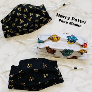 May include: Three Harry Potter themed face masks. One mask features a black background with gold triangle patterns. Another mask features a white background with colourful house crests. The third mask features a black background with gold glasses and lightning bolt patterns. The masks are all pleated and have elastic ear loops.