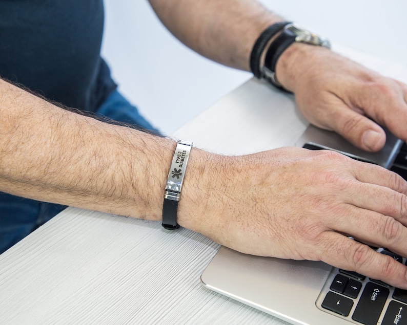 May include: A silver medical alert bracelet with the text "Type 2 Diabetes" and a star of life symbol. The bracelet is worn on a person's wrist.