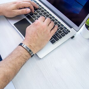 May include: A person wearing a black silicone bracelet with the text "MEDICAL ALERT" and a star of life symbol. The bracelet is on their left wrist.