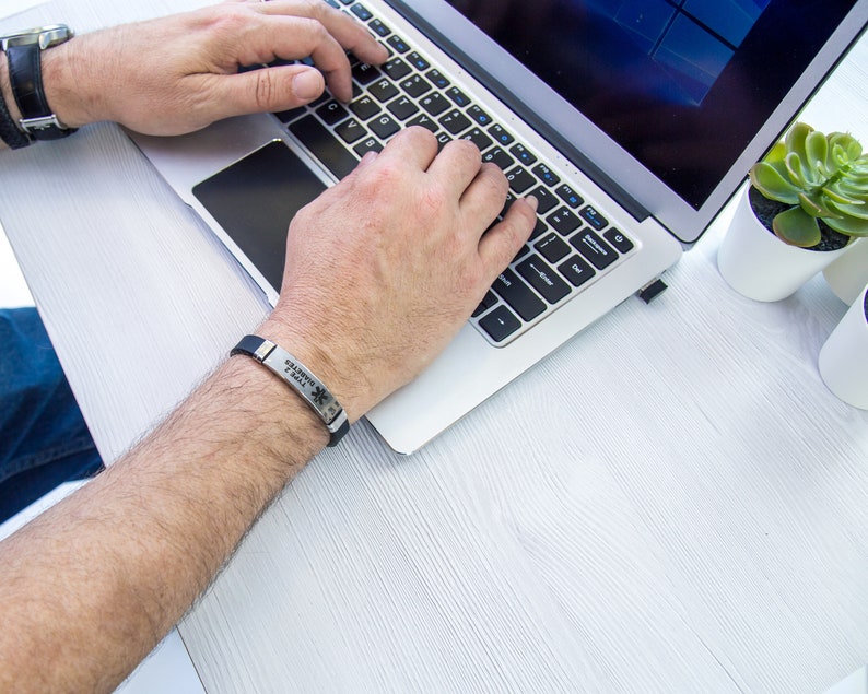 May include: A person wearing a black silicone bracelet with the text "MEDICAL ALERT" and a star of life symbol. The bracelet is on their left wrist.