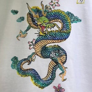 May include: A white t-shirt with a green, blue, and yellow dragon with pink flowers and clouds. The kanji character "力" is printed in a square in the top right corner.