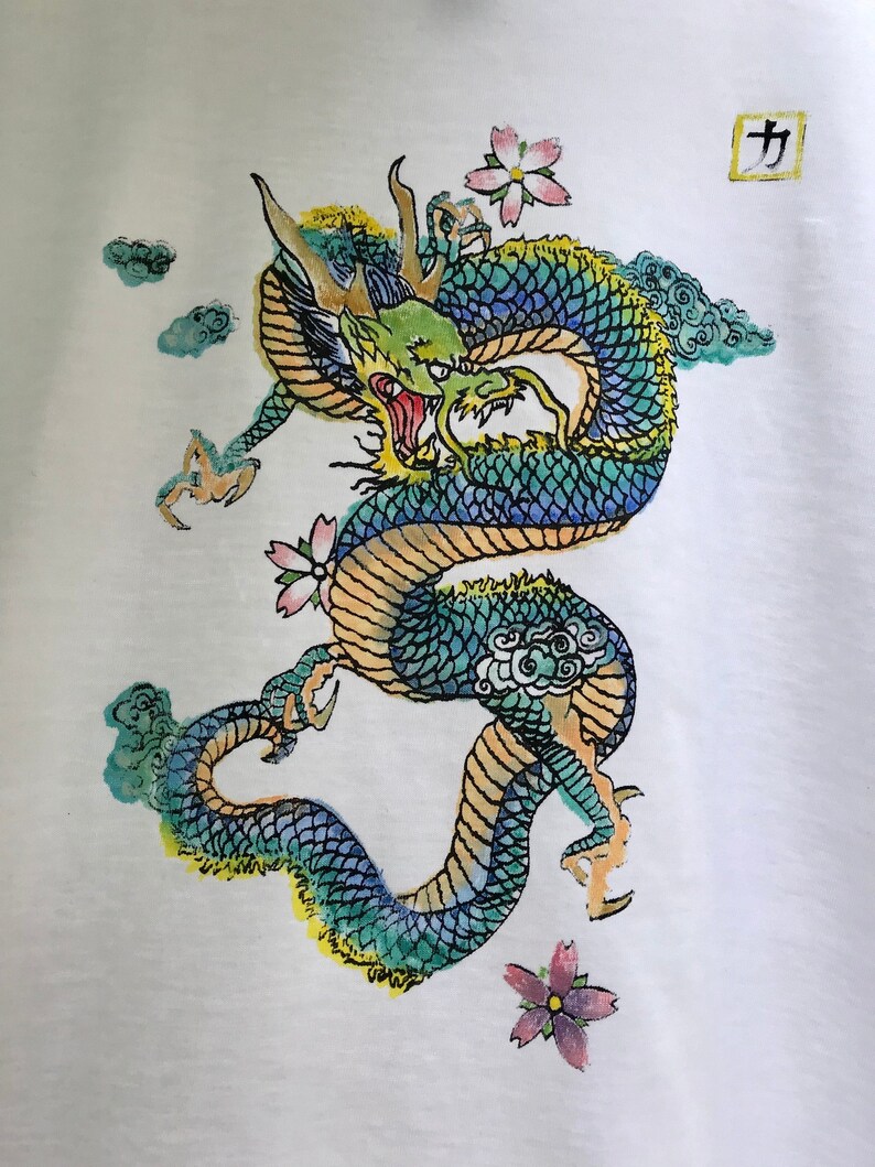 May include: A white t-shirt with a green, blue, and yellow dragon with pink flowers and clouds. The kanji character "力" is printed in a square in the top right corner.