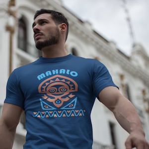 Puede incluir: Una camiseta azul marino con un diseño gráfico de una cara estilizada con la palabra "MAHALO" encima.