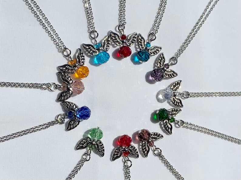 May include: A collection of angel wing pendant necklaces with various colored crystal beads. The pendants are silver-toned with detailed wings and a small crystal bead at the center. The necklaces are arranged in a circular pattern.