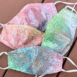 May include: Four face masks in various colors: pink, orange, green, and blue. Each mask has a shimmering, mosaic-like pattern and white adjustable ear loops. The masks are made of a shiny, iridescent material.