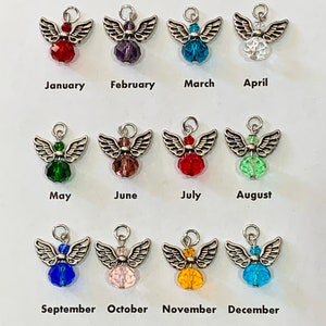 May include: A collection of twelve angel charms, each representing a month of the year. Each charm features silver-colored wings and a colored crystal bead. The months are labeled below each charm in black text.