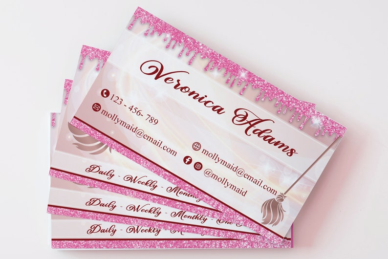 May include: Stack of pink and white business cards with a pink glitter border. The text on the card reads "Veronica Adams" and includes a phone number, email address, and social media handles. The card also features a gold broom with a pink glitter handle.