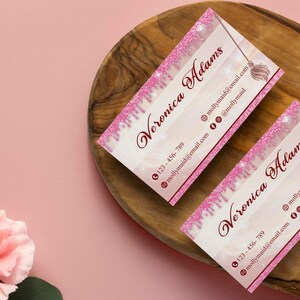 May include: Two pink and white business cards with a pink glitter design. The cards feature the name "Veronica Adams" and a phone number, email address, and social media icons.
