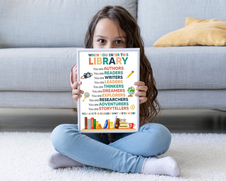 May include: A white sign with colorful text that reads "When you enter this library, you are..." and lists a variety of roles, such as authors, readers, writers, leaders, thinkers, dreamers, explorers, researchers, adventurers, and storytellers. The sign also includes a small illustration of a camera, magnifying glass, globe, and clock. The sign is held by a young girl wearing blue jeans.