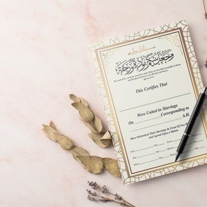 May include: A white and gold Islamic marriage certificate with Arabic calligraphy and a black pen on a pink surface.