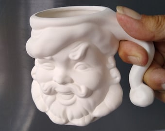 Könnte beinhalten: Ein unbemalter Keramikbecher in Form des Gesichts des Weihnachtsmanns. Der Becher hat ein detailliertes Design des Gesichts des Weihnachtsmanns, einschließlich Hut, Bart und lächelndem Ausdruck. Der Griff hat eine gebogene Form. Bereit zum Bemalen und Personalisieren.
