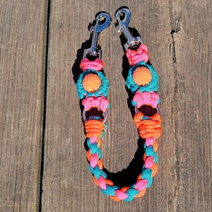 May include: A pink, teal, and orange braided dog leash with two silver clips and orange beaded accents.