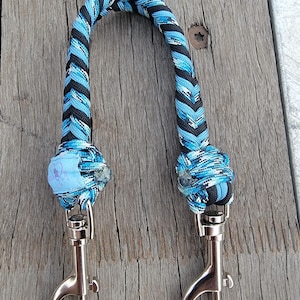 May include: A blue and black braided dog leash with two silver swivel clips. The leash is made of paracord and has a blue and white heart with the text "Love My Dog" on it.