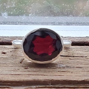 May include: A silver ring with a large, oval-shaped, dark red gemstone.