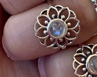 May include: A silver ring with a delicate floral design and a round, iridescent moonstone center.