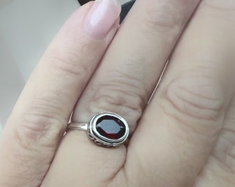 May include: A silver ring with a dark red oval gemstone set in a decorative silver bezel.