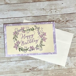 Cartão de felicitações de feliz aniversário floral com fio bordado lilás lavanda flores roxas folhas verdes com fundo de rosas roxas