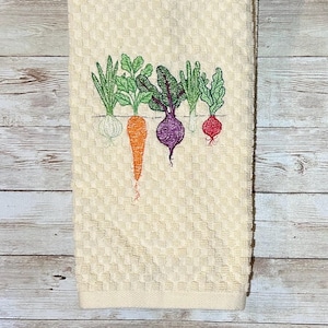 May include: A white kitchen towel with an embroidered design of five vegetables: a green onion, a carrot, a beet, a turnip, and a radish.