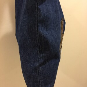 May include: A blue denim tote bag with a gold embroidered design on the side.
