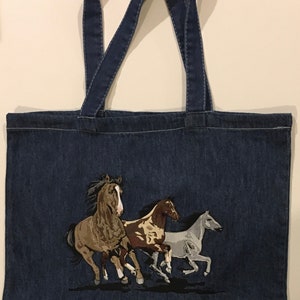 May include: A blue denim tote bag with an embroidered design of three horses running. The horses are brown, white, and brown and white.