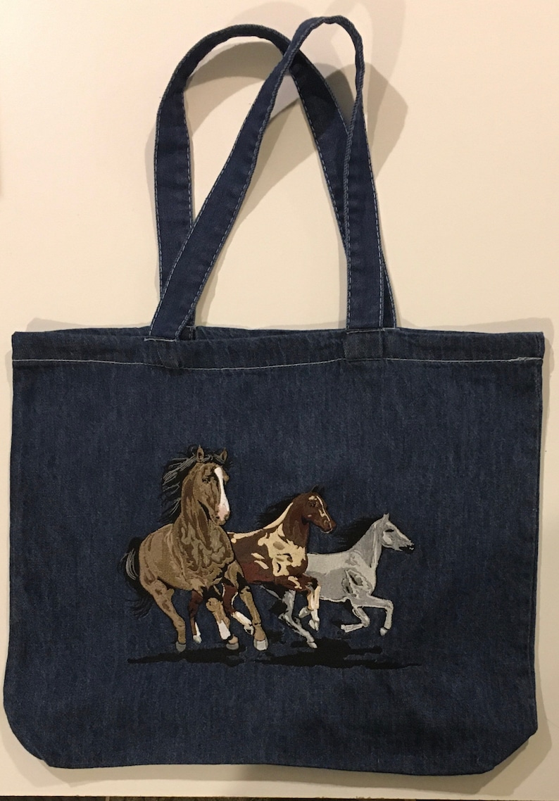May include: A blue denim tote bag with an embroidered design of three horses running. The horses are brown, white, and brown and white.
