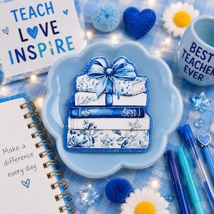 May include: A stack of five books tied with a blue ribbon bow, featuring floral and botanical patterns in shades of blue and white. The illustration is centered on a light blue scalloped dish, surrounded by stationery items and teacher-themed decor.