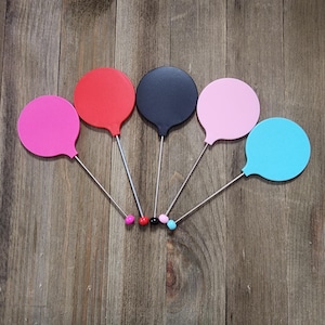 May include: Five colorful round balloon-shaped objects on sticks. The balloons are pink, red, black, light pink, and light blue. The sticks are silver with a small colored ball at the end.