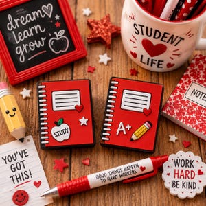 May include: Two red notebook-shaped pins featuring white spiral bindings, a lined paper graphic, and school-themed icons including an apple with the text STUDY and a pencil with the text A+. The pins are surrounded by school-themed stationery items.