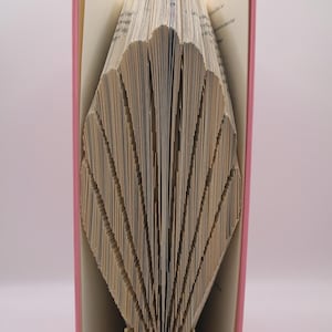 Może przedstawiać: Różowa książka ze stronami złożonymi w kształt muszli. Okładka książki jest różowa, a strony beżowe. Tekst "pattern only" jest widoczny na dole. To element dekoracyjny.