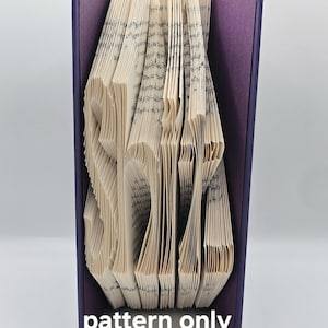 Pode incluir: Uma escultura de arte de livro em forma da palavra "SHINE" feita a partir das páginas de um livro. O livro é encadernado em uma capa roxa. A escultura é apenas um padrão, não um produto acabado.