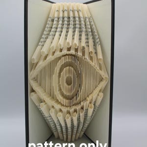 May include: A book folding pattern for an eye design. The pattern is printed on a white sheet of paper and is ready to be used to create a book folding art project.
