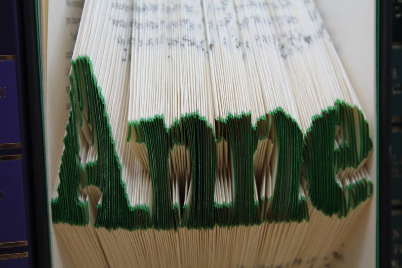 Puede incluir: Un libro doblado en forma del nombre "Alice" con bordes verdes. El libro est&aacute; doblado de forma que crea un efecto 3D.