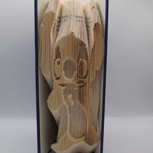 May include: A book with blue covers and pages folded to create a 3D image of the Disney character Stitch. The text "pattern only" is visible at the bottom of the book.