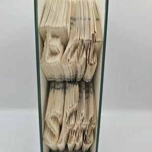 Pode incluir: Um livro com páginas dobradas em um design 3D da palavra "LOVE". O livro é encadernado em uma capa verde escura e o texto "pattern only" é impresso abaixo do design.